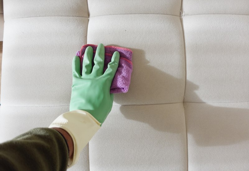 Hand wearing a glove is cleaning light-colored upholstered fabric with a cloth in Edmonton, AB